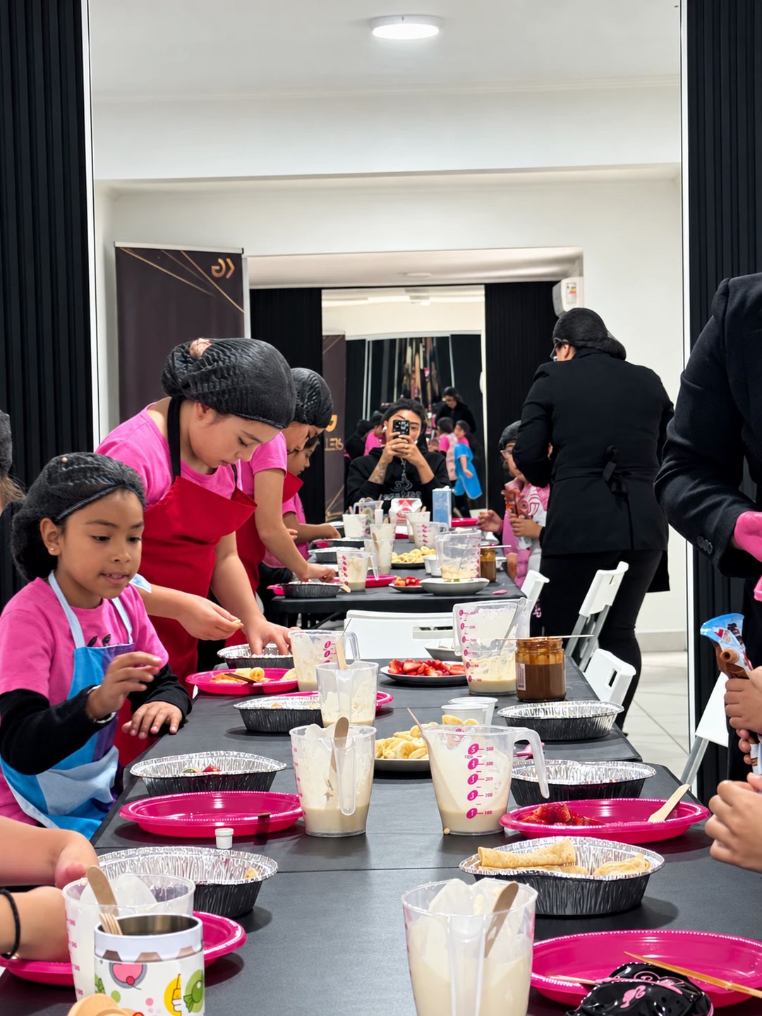Niñas de Kids con delantal y gorro preparando panqueques con fruta en el taller de cocina de Gallers